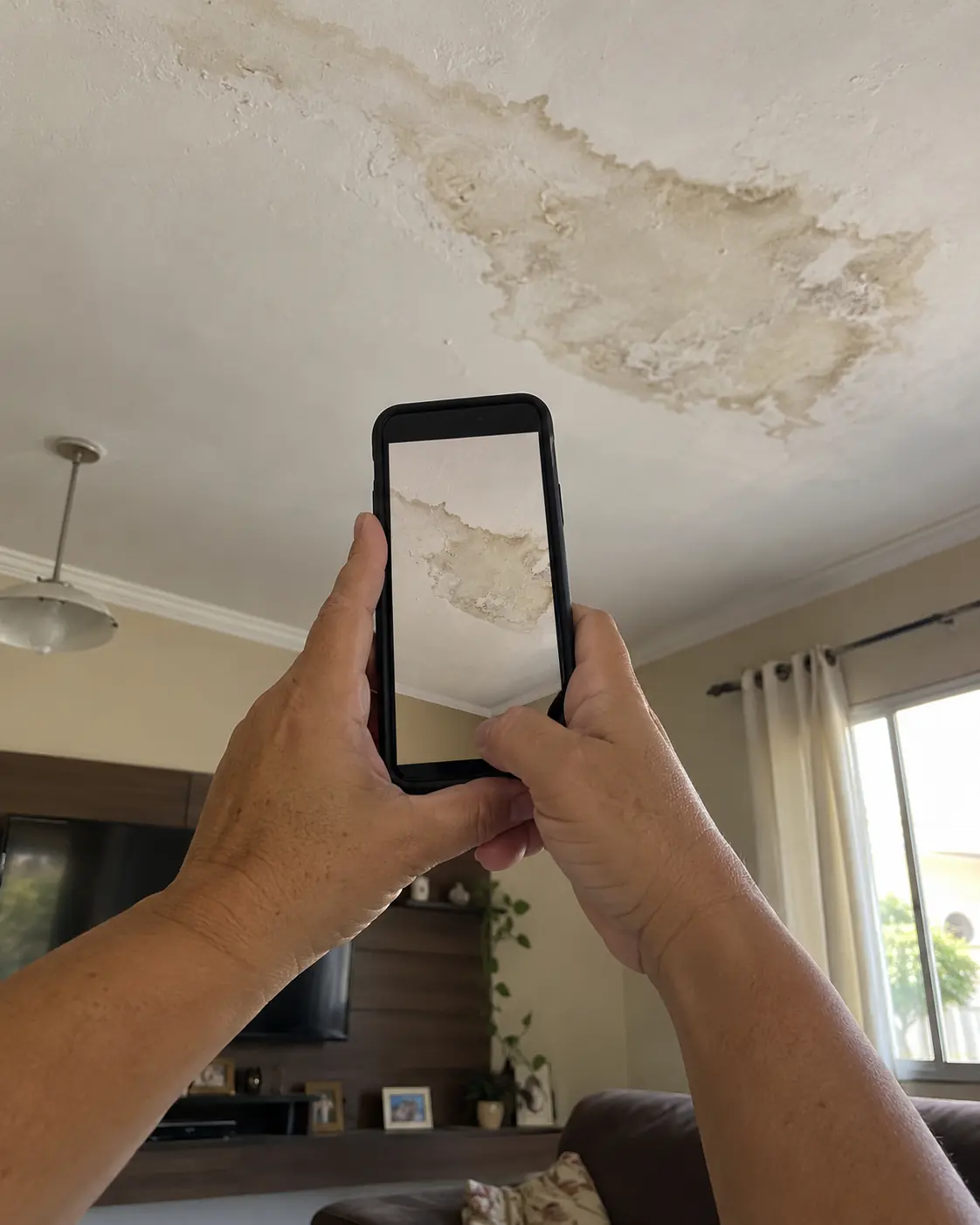 Mão segurando o celular e fotografando uma mancha no teto